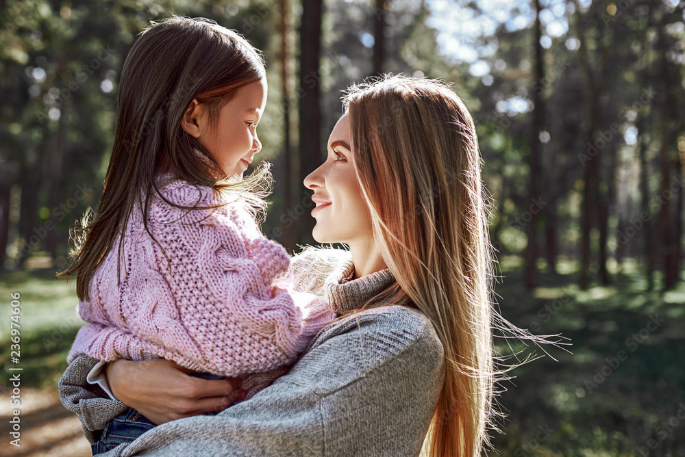 Happy, stylish little curly girl is hugging her beautiful mother in forest Happy, stylish little curly girl is hugging her beautiful mother in forest