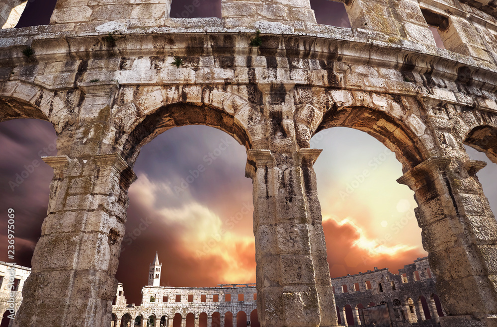 Famous Croatian city Pula old amphitheater arches with sunset sky background. Traveling in Europe concept.