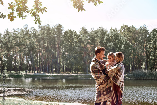 Young parents hugg their little daughter in autumn forest near the lake. photo