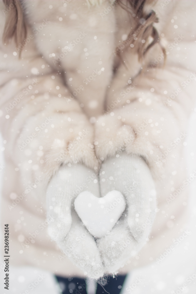 Fototapeta premium Woman hands are holding a beautiful glossy heart in a snow winter background. Love and St. Valentine cozy concept.