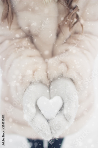 Woman hands are holding a beautiful glossy heart in a snow winter background. Love and St. Valentine cozy concept.