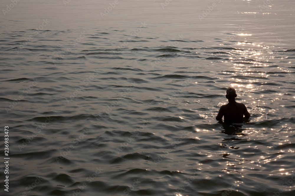 Silhouette of a man taking bath in ganges river during sunset