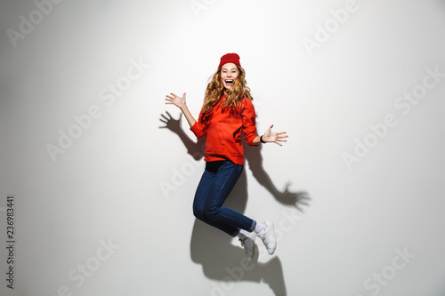 Full length photo of brunette woman 20s wearing red clothes laughing while jumping, isolated over white background