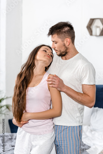 boyfriend in pajamas hugging girlfriend and couple going to kiss in bedroom