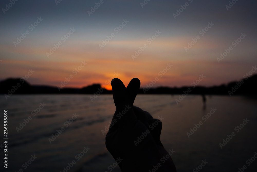 silhouette mini heart hand in sunset sky and sea beach