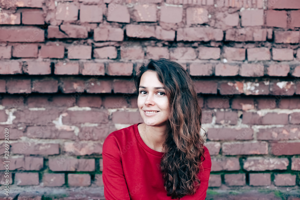 fashionable young girl with long hair, red sweater in. Model on brick wall background. fashionable young girl with long hair, red sweater in. Model on brick wall background.