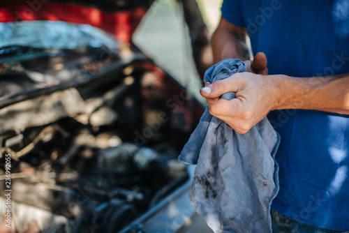 Man wipes his hands with a cloth in front of car