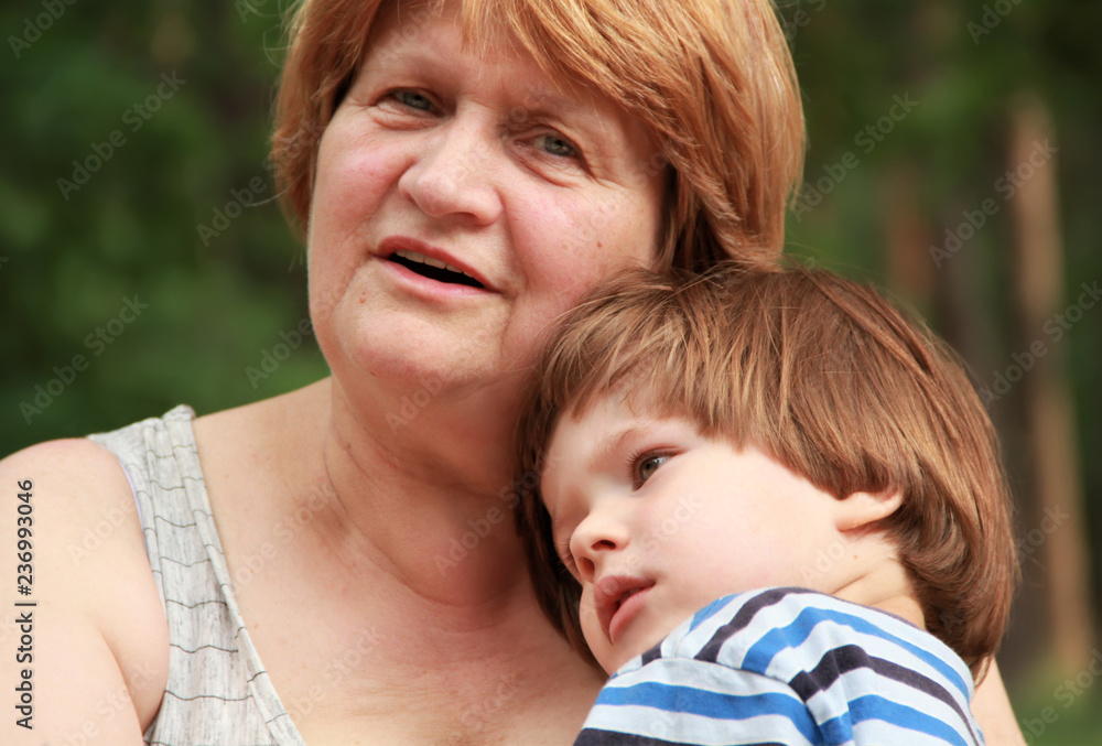 Happy grandmother is cuddling her grandson on a picnic in the forest. Close up portrait of a lady in her 60s Happy grandmother is cuddling her grandson on a picnic in the forest. Close up portrait of a lady in her 60s