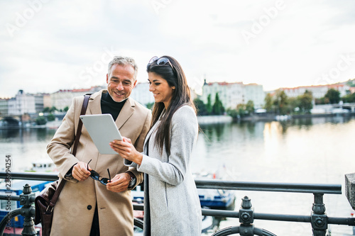 Canvas Print Man and woman business partners with tablet standing by a river in city of Prague