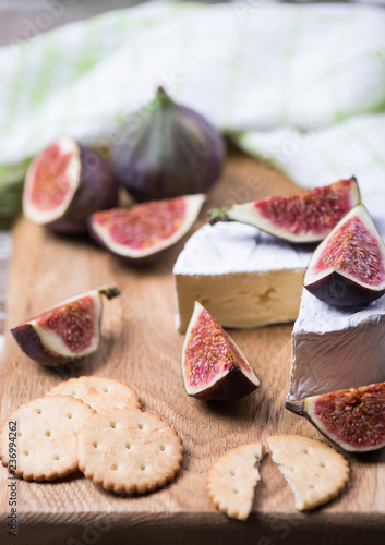 Ripe fresh figs fruits, cheese, cracker on a wooden board with textile towel.