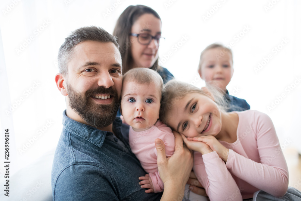 A portrait of young family with small children sitting indoors on a sofa.