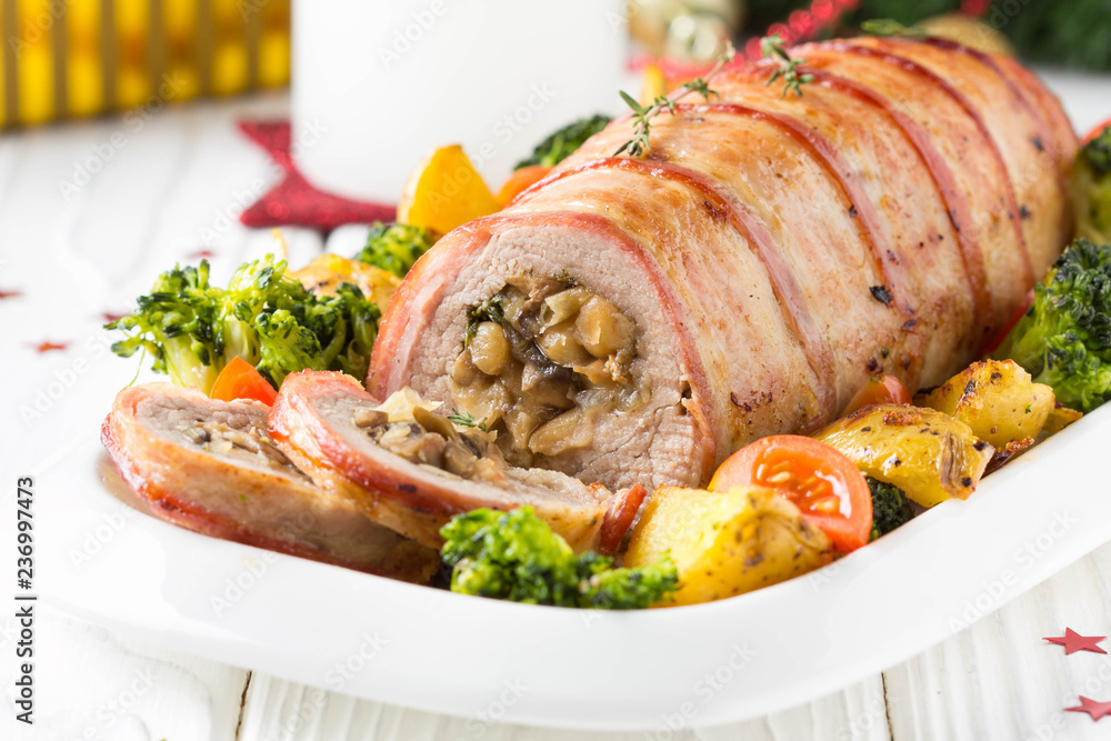 Pork roll wrapped in bacon stuffed with mushrooms and beans, vegetables on the side. Beautiful festive main dish for Christmas holidays Pork roll wrapped in bacon stuffed with mushrooms and beans, vegetables on the side. Beautiful festive main dish for Christmas holidays