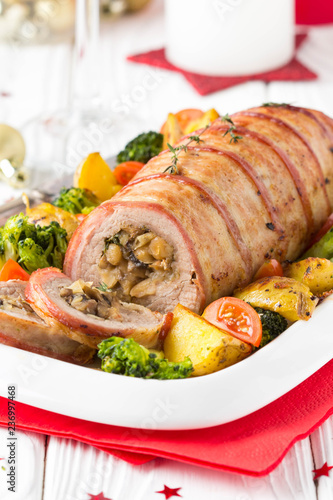 Pork roll wrapped in bacon stuffed with mushrooms and beans, vegetables on the side. Beautiful festive main dish for Christmas holidays photo