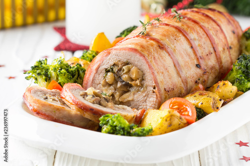 Pork roll wrapped in bacon stuffed with mushrooms and beans, vegetables on the side. Beautiful festive main dish for Christmas holidays
