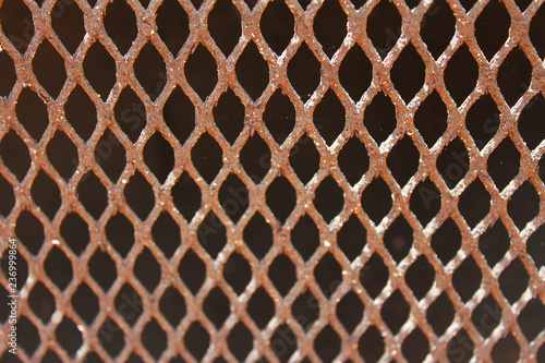 Close-up of steel grill. Steel is rusted. Focus is on top of image, diminishing moving down. Sunlight is shining on grill.