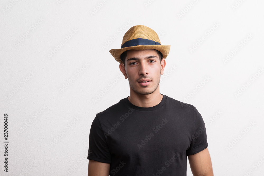 A confident hispanic young man with hat and black T-shirt in a studio.
