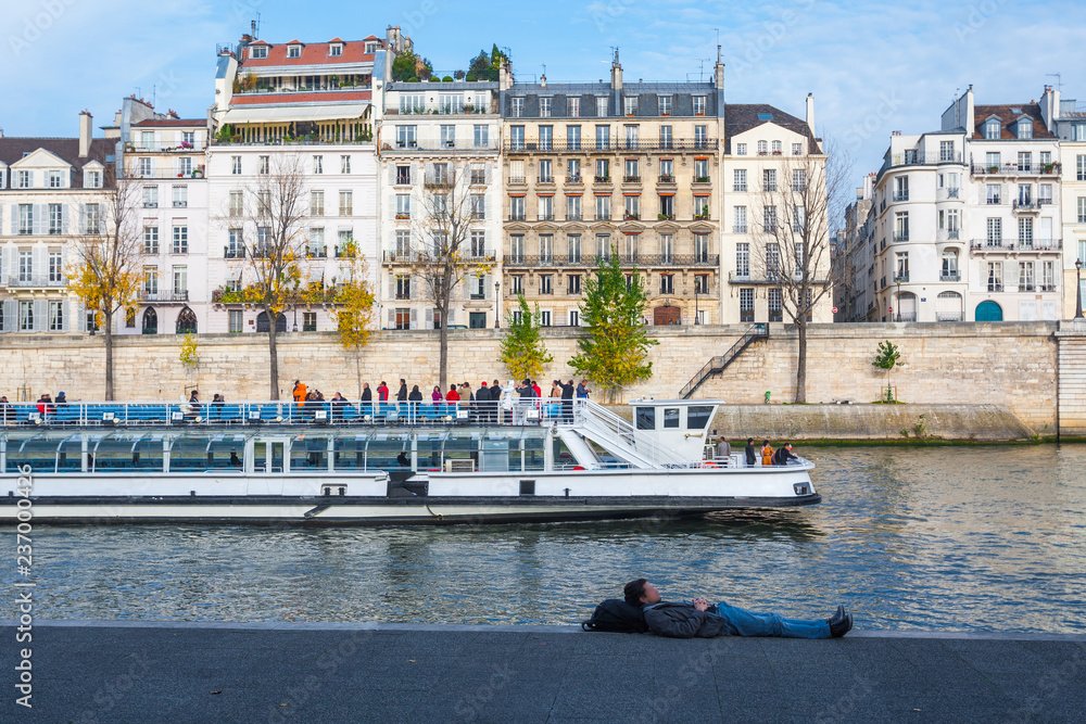 Embankment of the Seine at sunny autumn afternoon. Boat on scenic route. Tourists and natives a walk and relax in warm weather. Blurred unrecognizable faces. Paris. France.