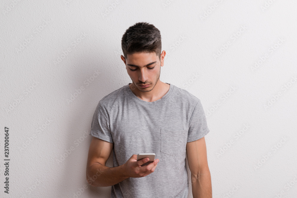 Young hispanic man with smartphone standing in a studio, text messaging. Young hispanic man with smartphone standing in a studio, text messaging.