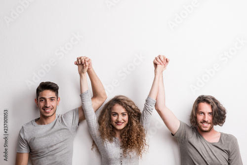 Portrait of joyful young girl with two boy friends standing in a studio, lifting hands.