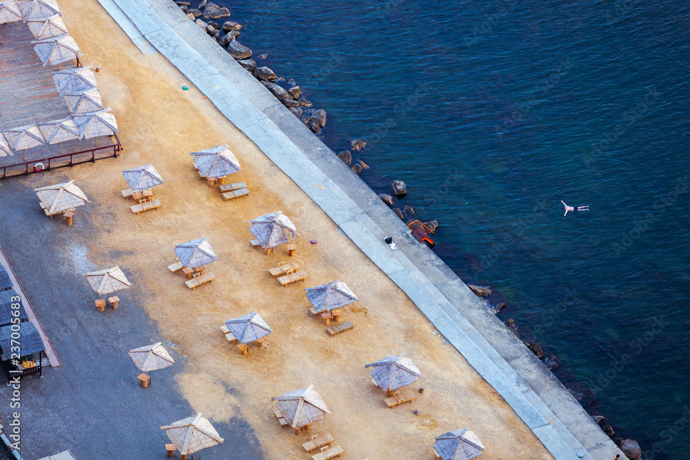 Aerial view of beach with umbrellas and blue sea water with one person alone swimming in water