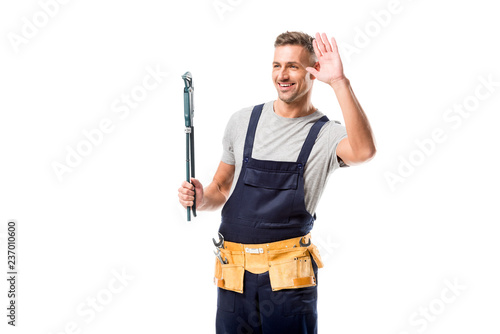 happy worker holding pipe wrench, waving and looking away isolated on white