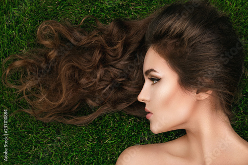 Beautiful woman with a healthy curly hair is lying on the grass