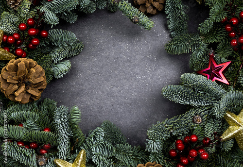 Christmas frame made of fir-tree branches, festive decorations, and cones on the gray background