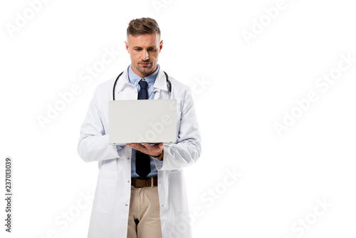 focused doctor in white coat using laptop isolated on white