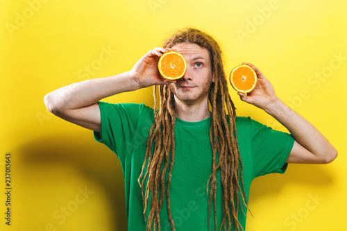 Happy young man holding oranges on a yellow background