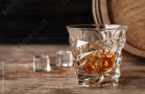 Golden whiskey in glass with ice cubes on wooden table. Space for text