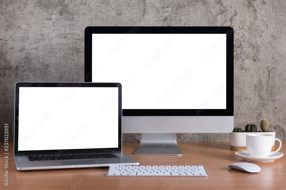 Fototapeta premium Blank screen of all in one computer and laptop computer with coffee cup and cactus vase on raw concrete background