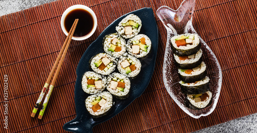 banner of vegan ready-made sushi on the table in fish plates. rolls with fried tofu, cucumber, boiled carrots and fresh avocado. healthy vegan food