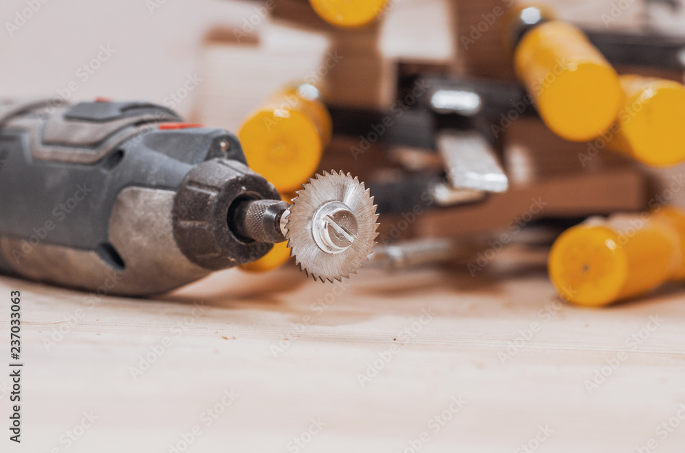 Dremel tool with an installed small circular saw on a wooden board background. Workshop. Manufacture of wooden products. Joiner's cutting tool Dremel tool with an installed small circular saw on a wooden board background. Workshop. Manufacture of wooden products. Joiner's cutting tool