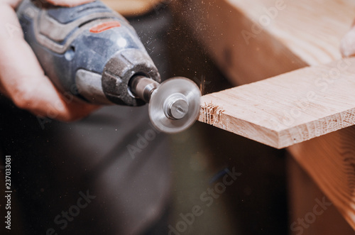 hands of a man holding a Dremel tool with an installed small circular saw. Wood processing. Workshop. Manufacture of wooden products. Joiner's cutting tool photo