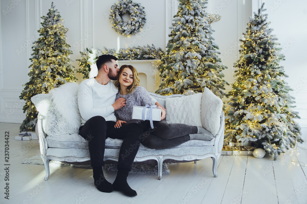 Obraz premium A couple in love gently smiling at each other, sitting on the sofa near the Christmas, New Year tree