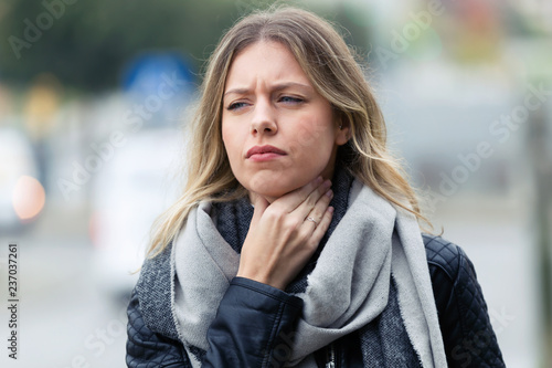Illness young woman with terrible throat pain walking to the street. photo