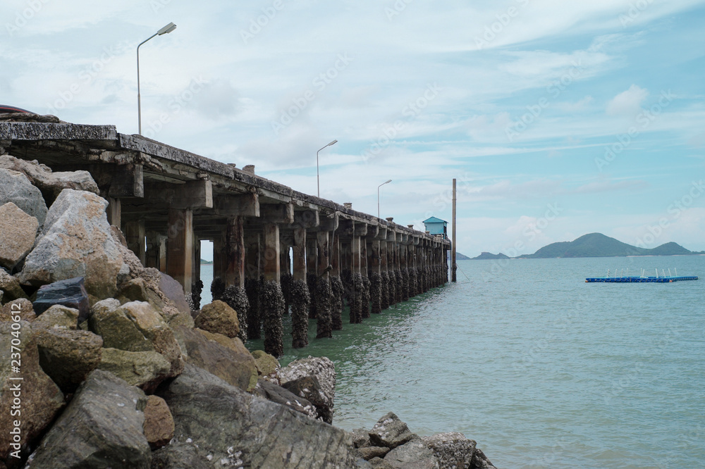Fototapeta premium Concrete road into the sea with landscape and island in background. Seascape and the port structureinto the sea.