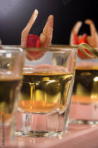 Close-up shot of three glasses of Golden tequila with tapas on skewers with dried meat, baked bell pepper and pine nuts.