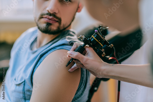 Attentive tattoo artist gently touching skin of her client with tattoo machine