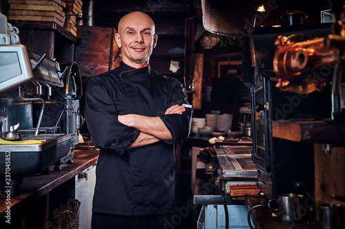 Foto Confident chef posing with his arms crossed and looking at a camera in restaurant kitchen
