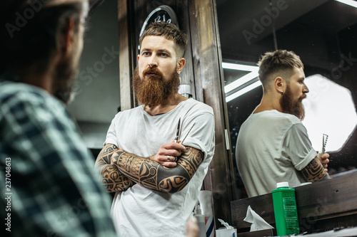 Waist up of thoughtful barber standing with crossed arms and looking