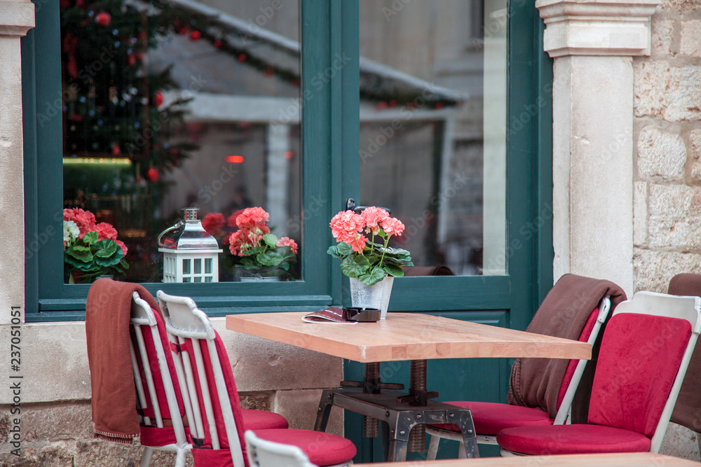 Street cafe at Christmas market in old town. Table and chairs with plaids near wooden window. Cozy festive atmosphere in Dubrovnik, Croatia. Street cafe at Christmas market in old town. Table and chairs with plaids near wooden window. Cozy festive atmosphere in Dubrovnik, Croatia.