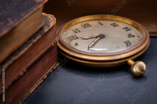 Panta rhei concept: antique pocket watch and pile of vintage hard cover books on natural stone background.