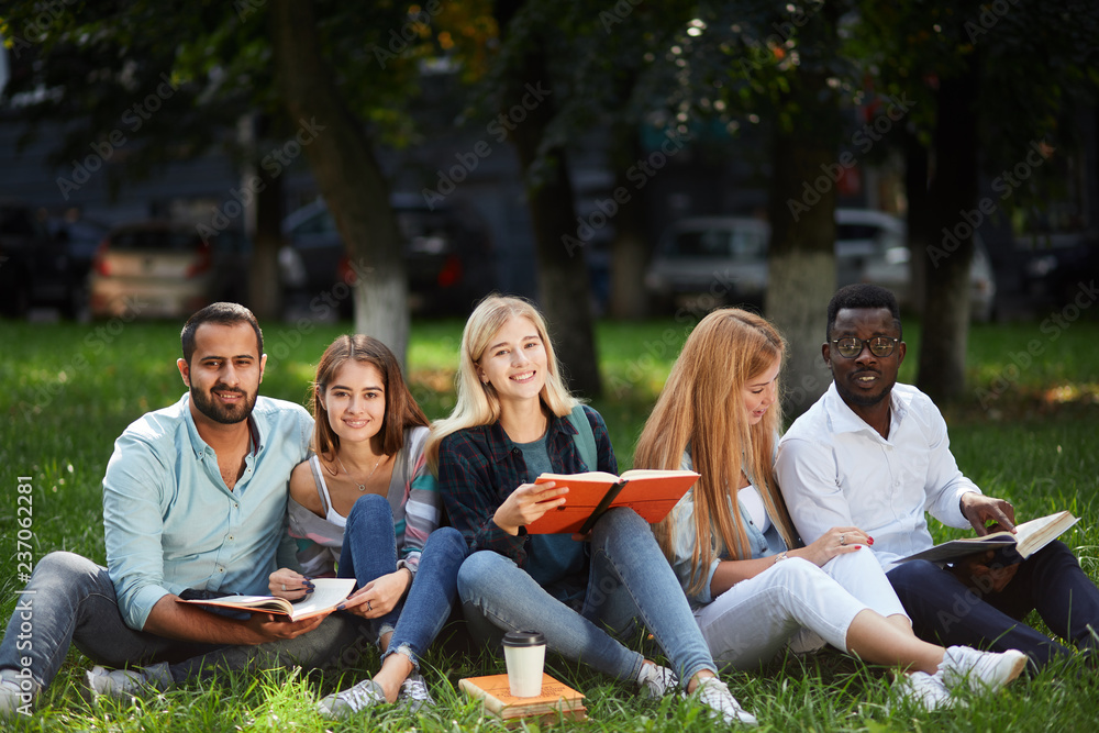 group of young students sitting together on green lawn high school university campus group of young students sitting together on green lawn high school university campus