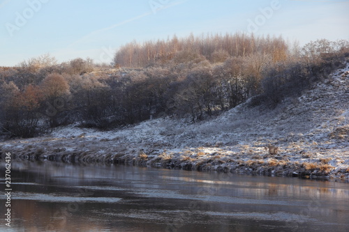 European river with a high Bank in sunny morning at the beginning of winter against the forest covered with frost on the horizon - the first snow, frost, beautiful water landscape