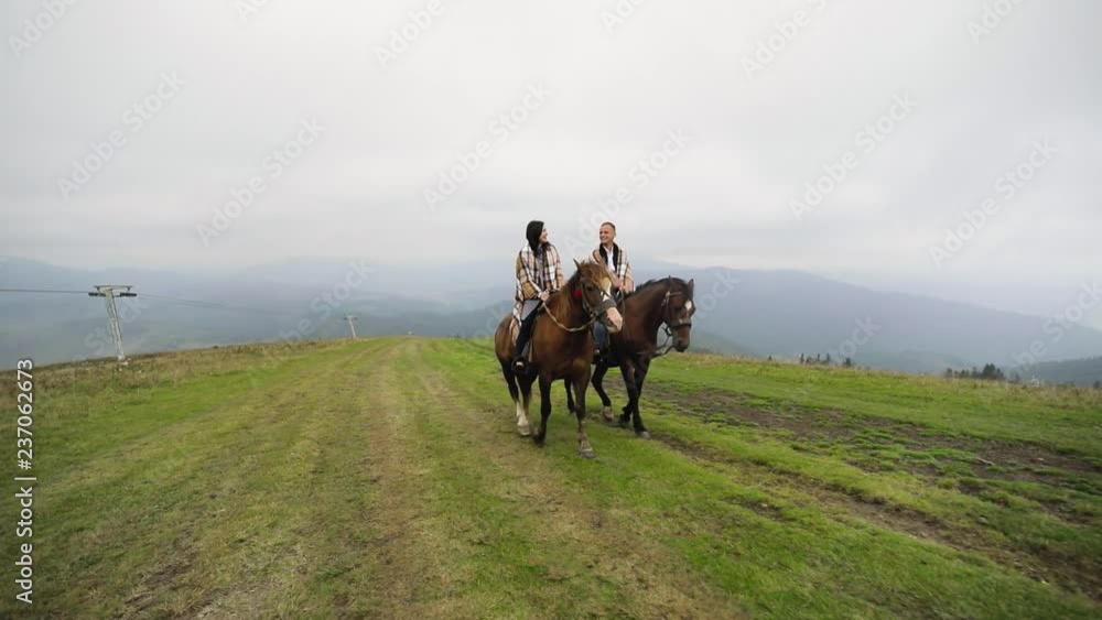 Beautiful couple ride horses in mountains in cloudy weather Beautiful couple ride horses in mountains in cloudy weather