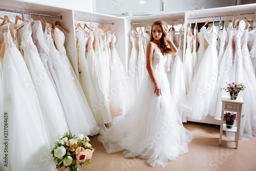 Fotografija Back view of a young woman in wedding dress looking at bridal gowns on display i