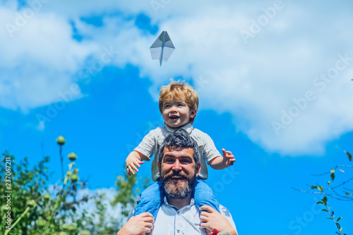 Happy father with son playing with toy plane. Dream to be pilot. Father with child have fun joy on nature at day time. Boy with toy aeroplane sitting on fathers shoulders at park. Family happy travel