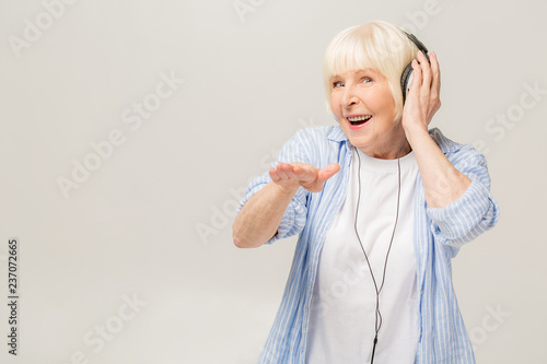 Elderly cheerful woman with headphones listening to music on a phone isolated on white background.