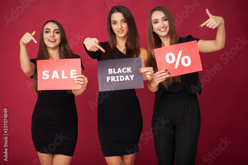 Shopping. Three women holding discount blank on red background in black friday holiday